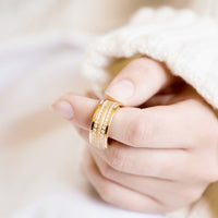 Curled Hand Resting on Lap Elegant Triple Yellow Gold 9mm Spinner Ring with Cubic Zirconia and Sparkling Texture on Pointer Finger