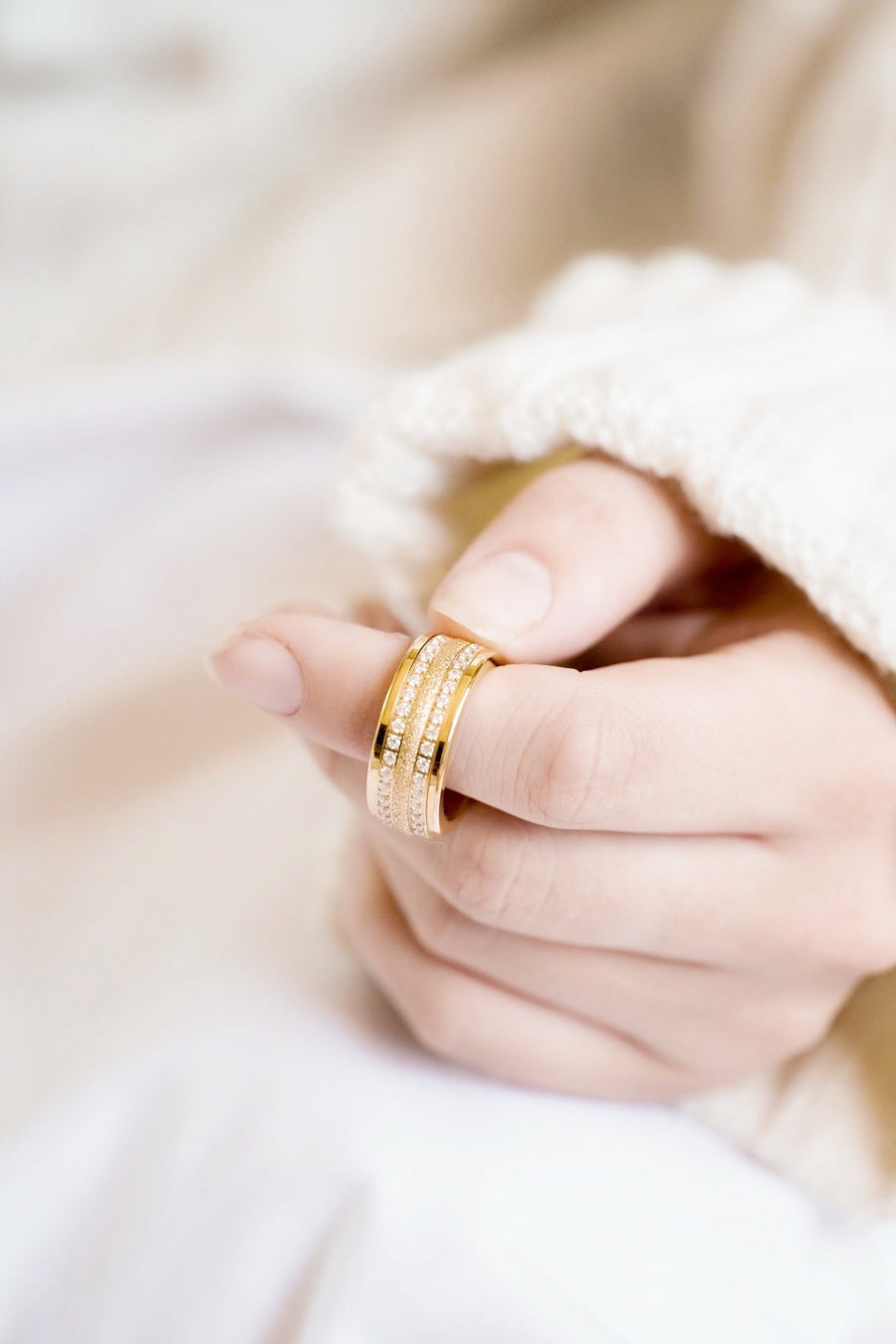 Curled Hand Resting on Lap Elegant Triple Yellow Gold 9mm Spinner Ring with Cubic Zirconia and Sparkling Texture on Pointer Finger