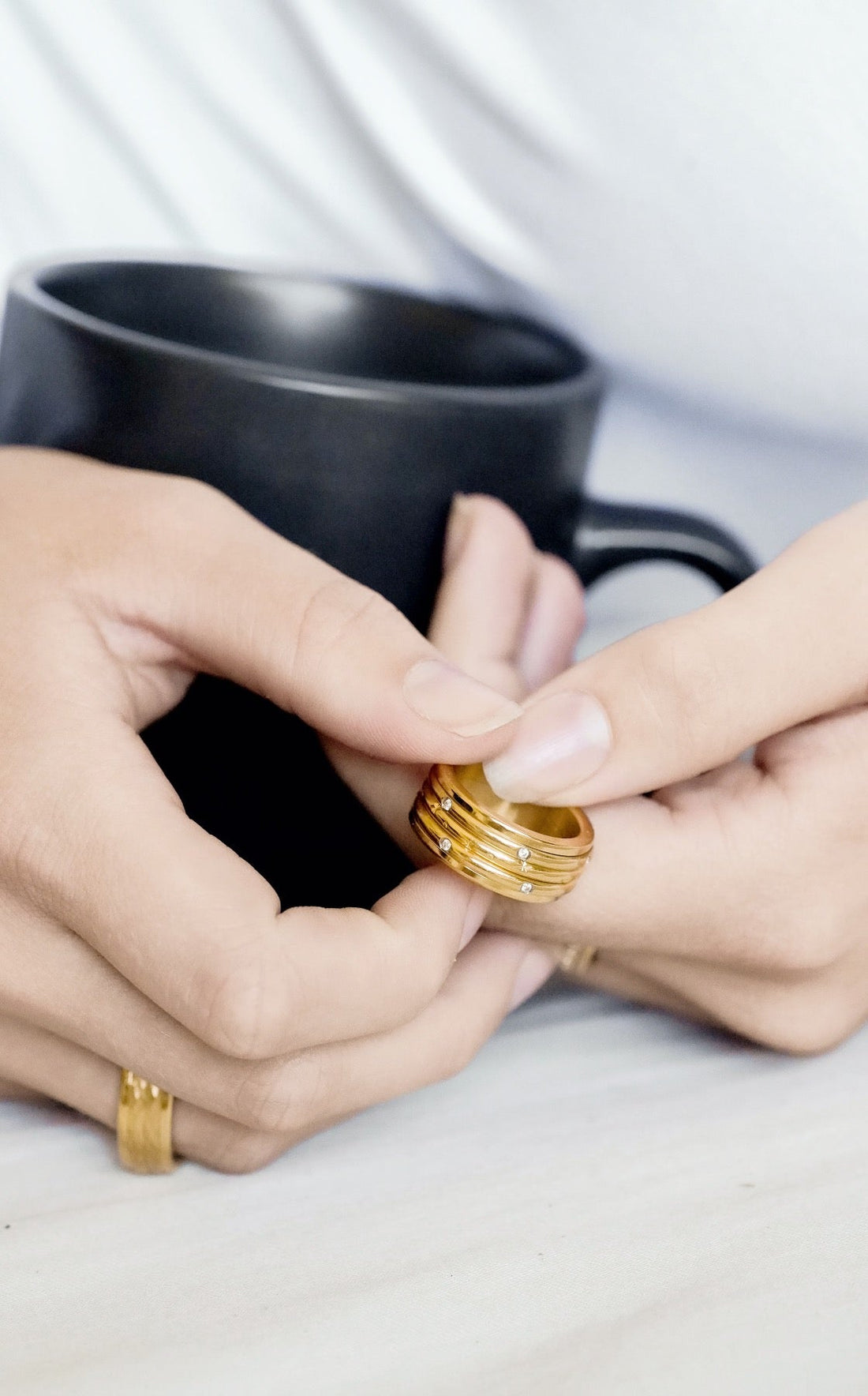 Hands cupping black coffee mug and golding gold spinner anxiety ring with moon and stars