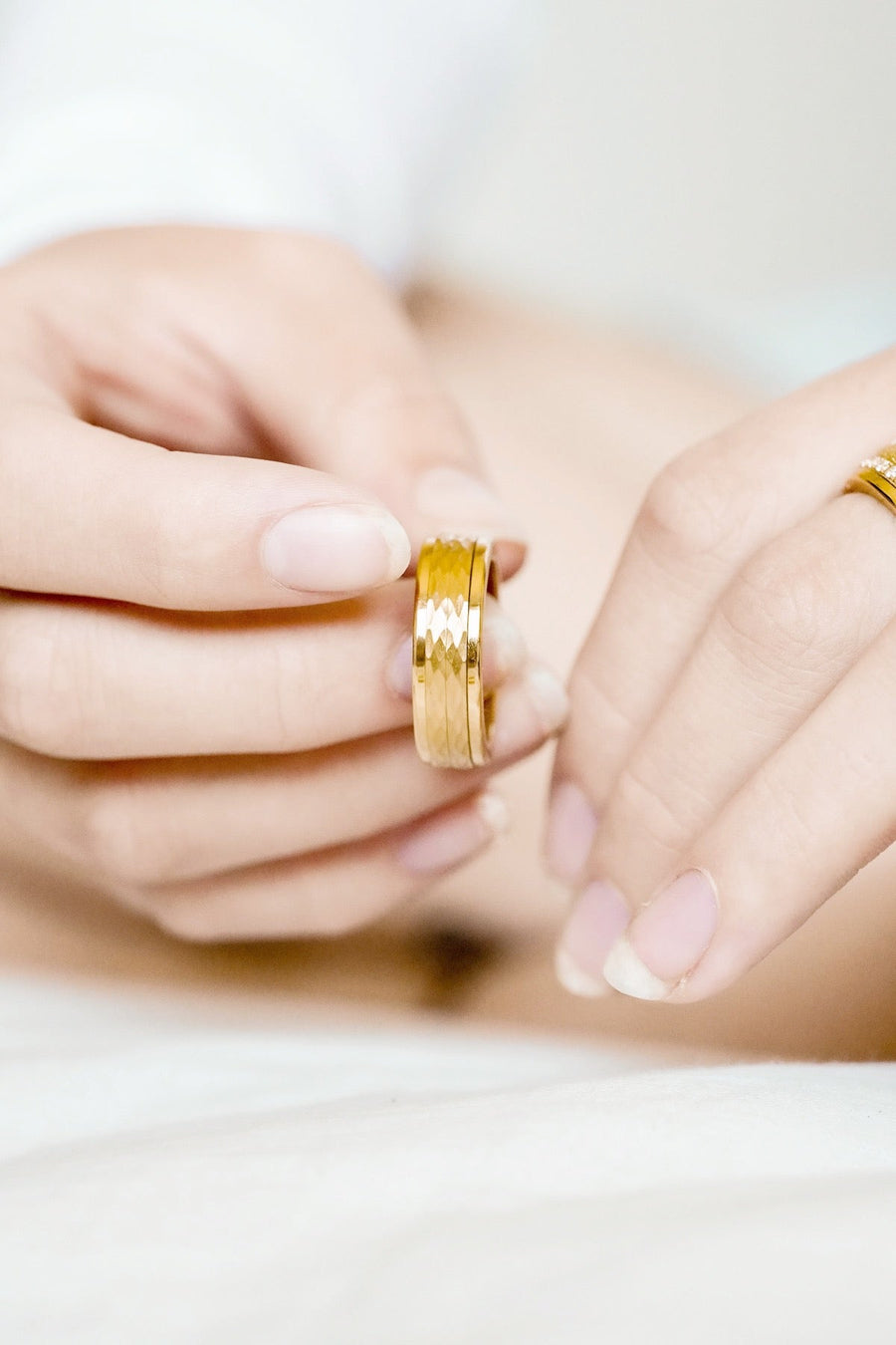 pair of hands clasping Textured 7mm Yellow Gold Double Spinner Ring between fingers