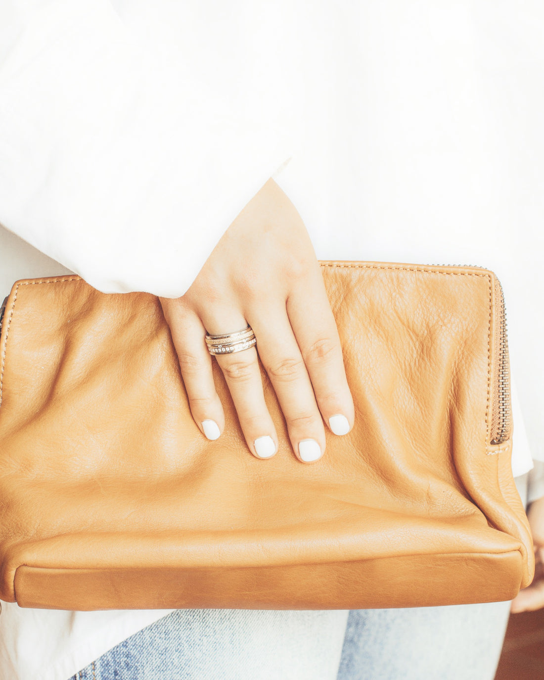 Right hand clasping tan leather clutch wearing Tricolour Triple Spinner Anxiety Ring with Sparkling Texture on ring finger