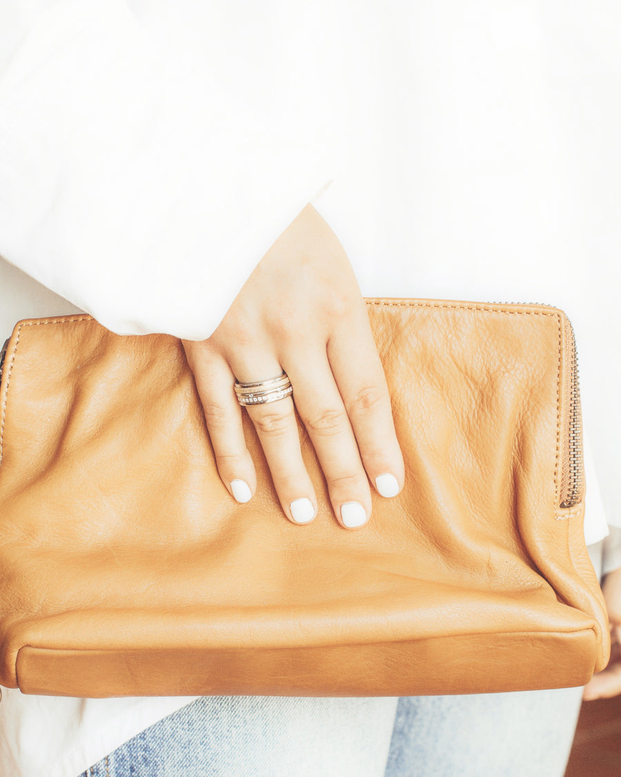 Right hand clasping tan leather clutch wearing Tricolour Triple Spinner Anxiety Ring with Sparkling Texture on ring finger